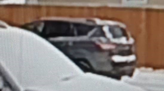 A blurry image of a dark-coloured SUV with some snow on parts of the back of the trunk