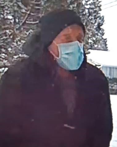 A man wearing a dark toque and dark jacket wearing a blue medial face mask