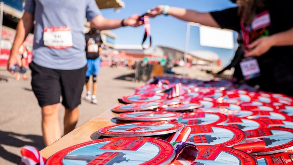 A Calgary Marathon volunteer hands a runner a medal at a table covered in hardware