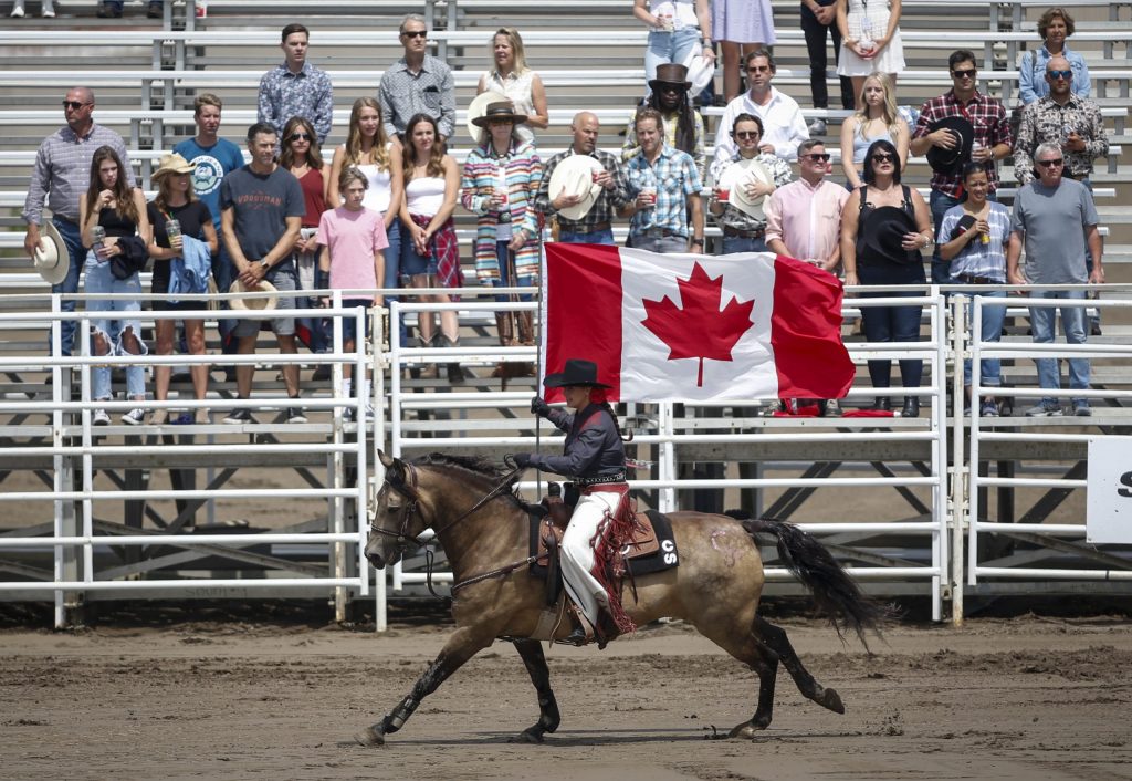 A rider carries the Canadian flag during the national anthem before the start of rodeo action at the Calgary Stampede