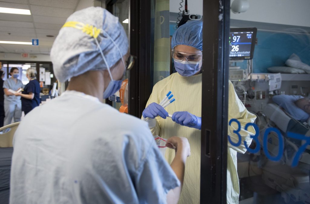 Nurses collect samples from a patient in a COVID suspect room