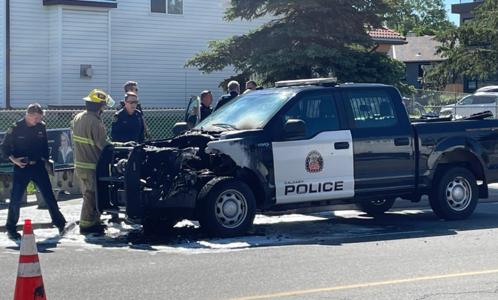 A Calgary police pick-up truck is tended to by firefighters and others after the front end caught fire. The vehicle's front is seen badly damaged