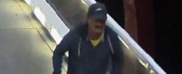 A close-up image from a CCTV camera of a man wearing a dark coloured ball cap and dark hoodie with yellow 