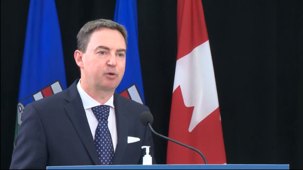 Alberta Health Minister Jason Copping speaks at a podium in front of the flags of Canada and Alberta