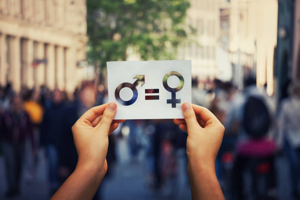 Gender equality concept as woman hands holding a white paper sheet with male and female symbol over a crowded city street background