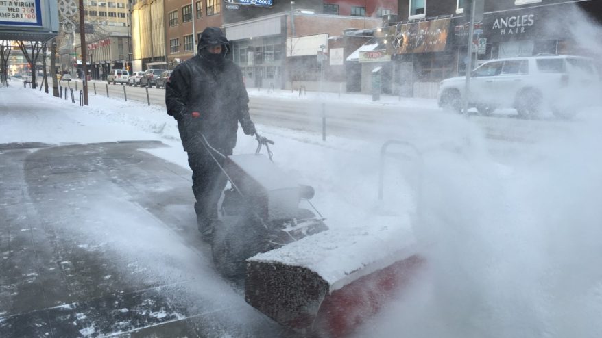 a picture showing someone clearing snow from a calgary sidewalk