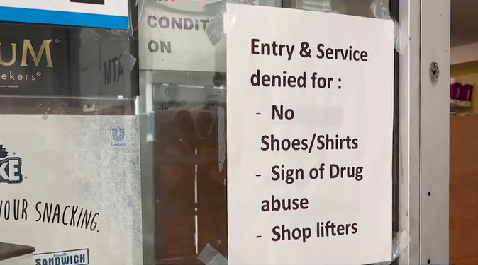 A sign on the glass door of a downtown business that reads: "Entry & Service denied for: - No Shoes/Shirts - Sign of Drug abuse - Shop lifters"