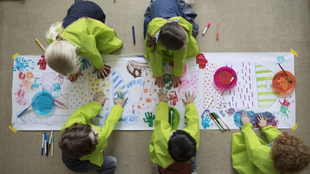 Overhead view community focused preschool students using finger paints on poster.