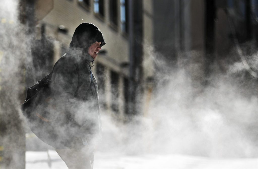 A man walks through steam venting from a building in the cold weather