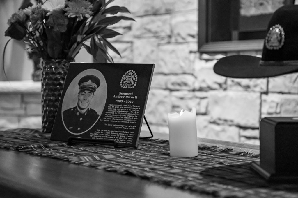 Flowers, a candle, a memorial plaque and hat sit on a countertop.