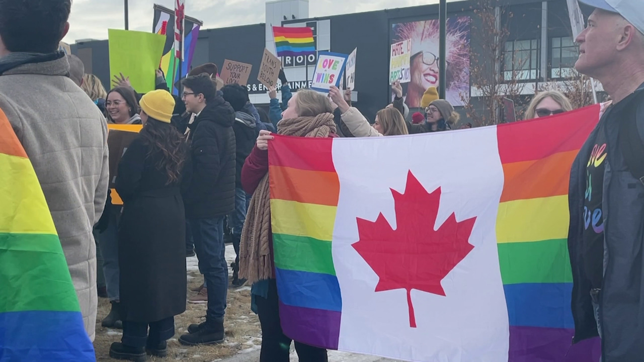 Calgarians hold up a Canadian flag with rainbow Pride colours in front of the Rec Room