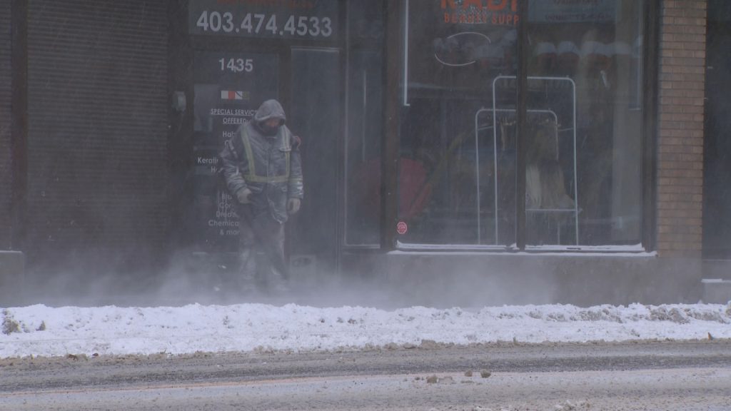 A person blows snow off a sidewalk in Calgary