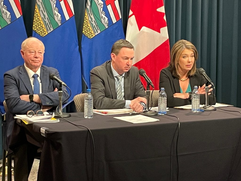 AHS Administrator John Cowell, left, sits with Health Minister Jason Copping, centre, and Alberta Premier Danielle Smith sit at a news conference at the McDougall Centre in Calgary