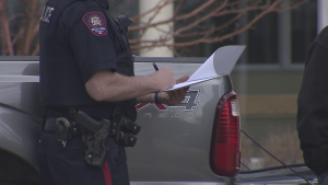 a calgary police officer looks at a clipboard outside of a crime seen that saw two people dead