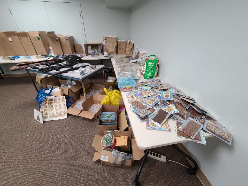 A far shot of seized illegal edible cannabis products, pre made illegal cannabis cigarettes, and packaging materials