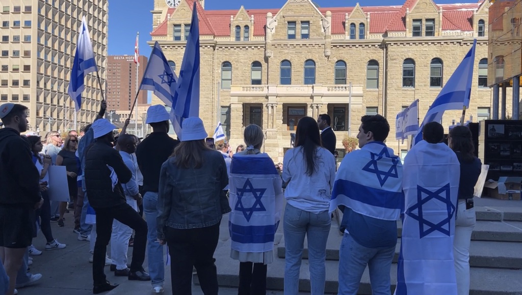 People with flags of Israel draped on their backs rally outside the Municipal building in Calgary