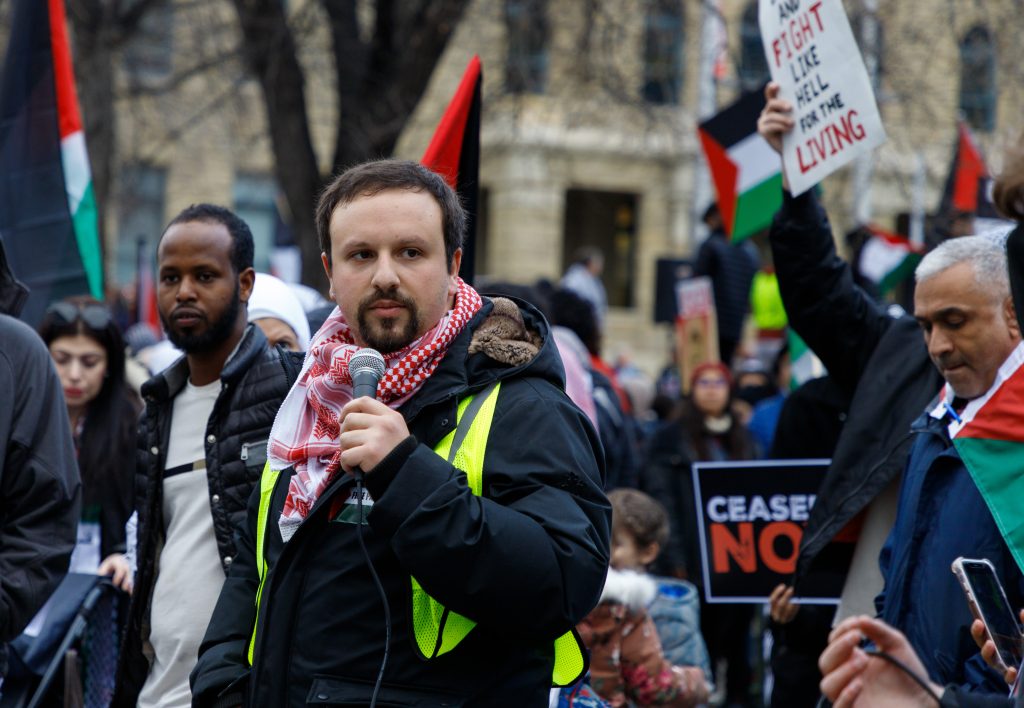 Wesam Cooley, organizer for Justice for Palestinians, holds up a microphone in front of the Municipal Building in Calgary