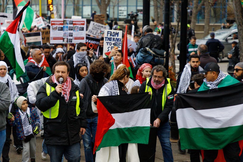 Wesam Cooley, left, speaks into a microphone as pro-Palestine protestors march onto Stephen Avenue in Calgary