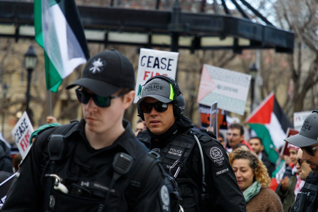 A police officer among pro-Palestine protestors as they march onto Stephen Avenue in Calgary