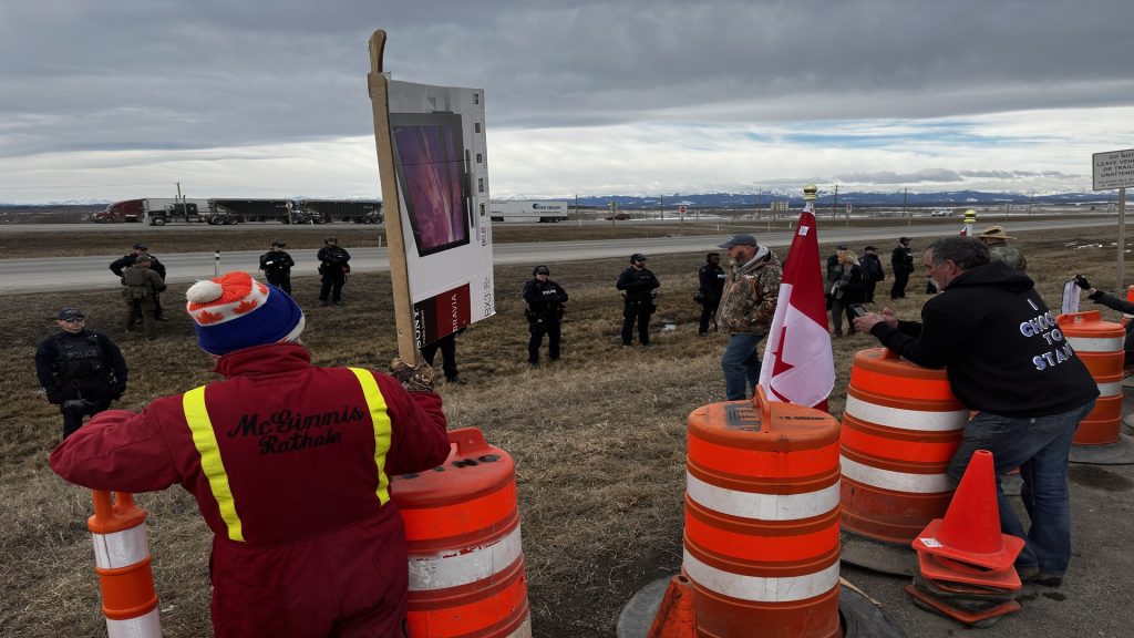 People protesting an increase to the federal carbon tax on April 1 line up along Highway 1 west of Calgary for a second day of demonstrations on April, 2, 2024, while RCMP stand in a line along the ditch. (Nick Blakeney, CityNews image)