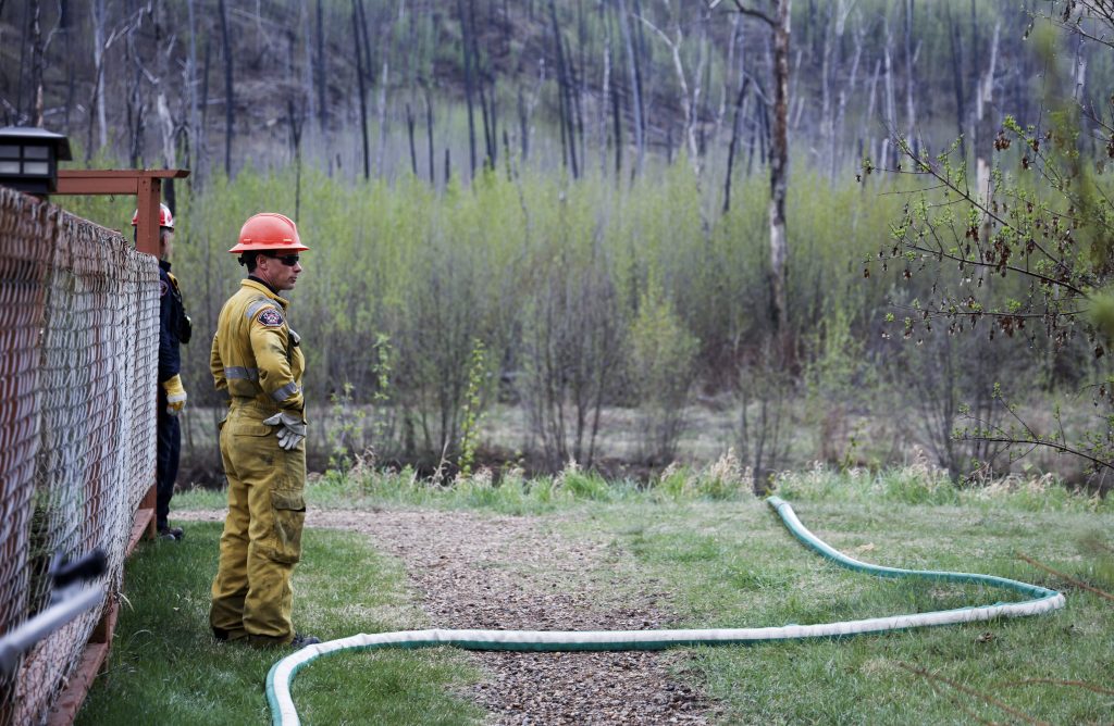 A firefighter monitors a wildfire sprinkler hose in the evacuated neighbourhood of Grayling Terrace in Fort McMurray, Alta., Thursday, May 16, 2024. Cool, wet weather over the past week has lowered the risk of wildfires in Alberta. THE CANADIAN PRESS/Jeff McIntosh Jeff McIntosh