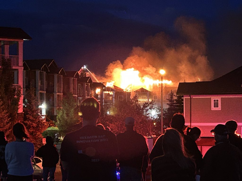 Onlookers watch as a fire burns a condo in Calgary's southeast on Sunday, June 23, 2024. (@gotrockseh1, X)