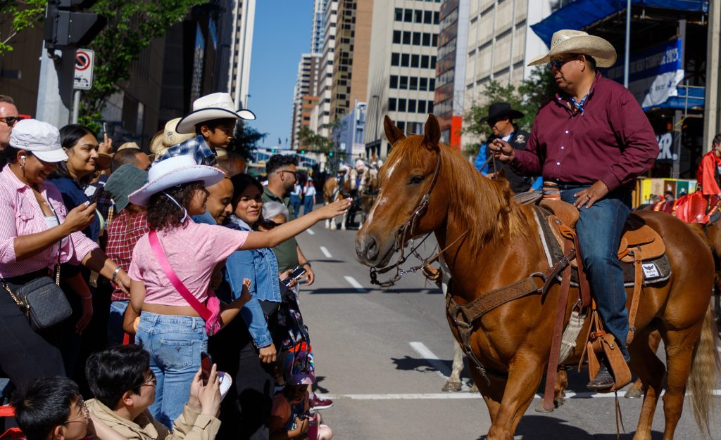 A child goes to pet a horse in the 2024 Stampede Parade kicksin downtown Calgary on Friday, July 5, 2024