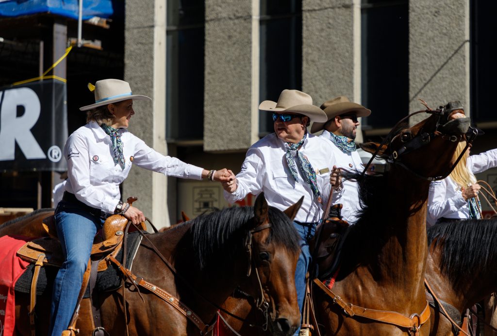 Steve McDonough, Immediate Past President of the Calgary Stampede, holds Mayor Jyoti Gondek's hand as his horse moves about at the 2024 Stampede Parade in downtown Calgary
