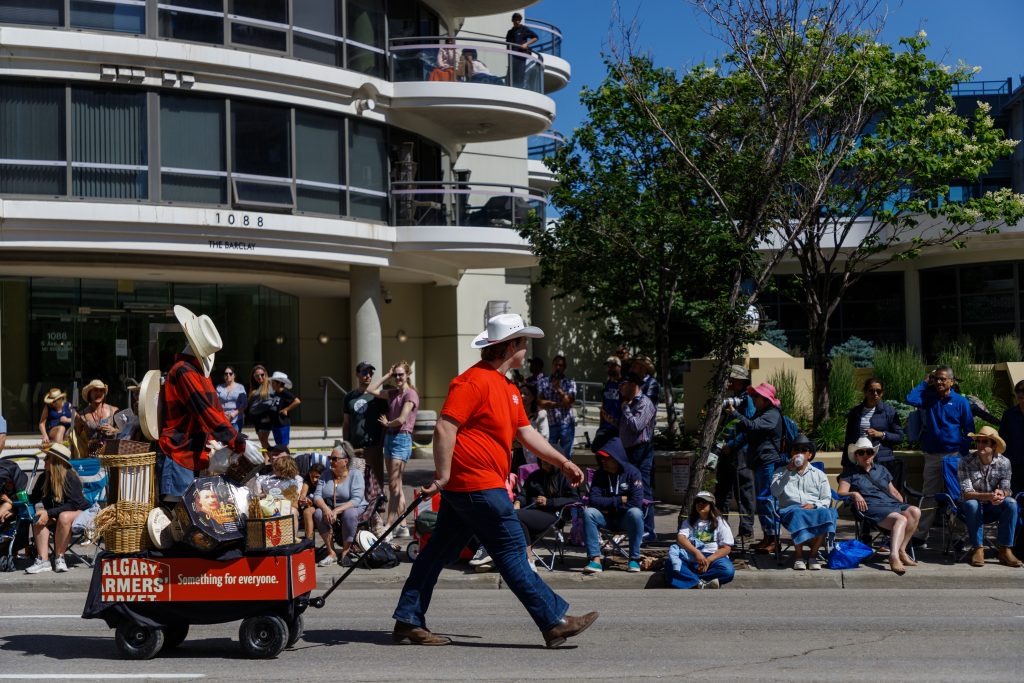 A member of the Calgary Farmers Market carries a wagon filled with goods in the 2024 Stampede Parade in downtown Calgary