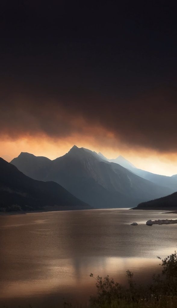 Smoke obscures the sky as the Rockies rise behind Medicine Lake in Jasper National Park