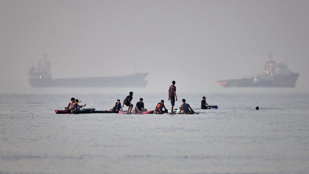 People gather on paddleboards in shallow water as cargo and service vessels are anchored in the Strait of Hormuz off Bandar Abbas, Iran, Monday, June 1, 2026. (Amirhosein Khorgooi/ISNA via AP)